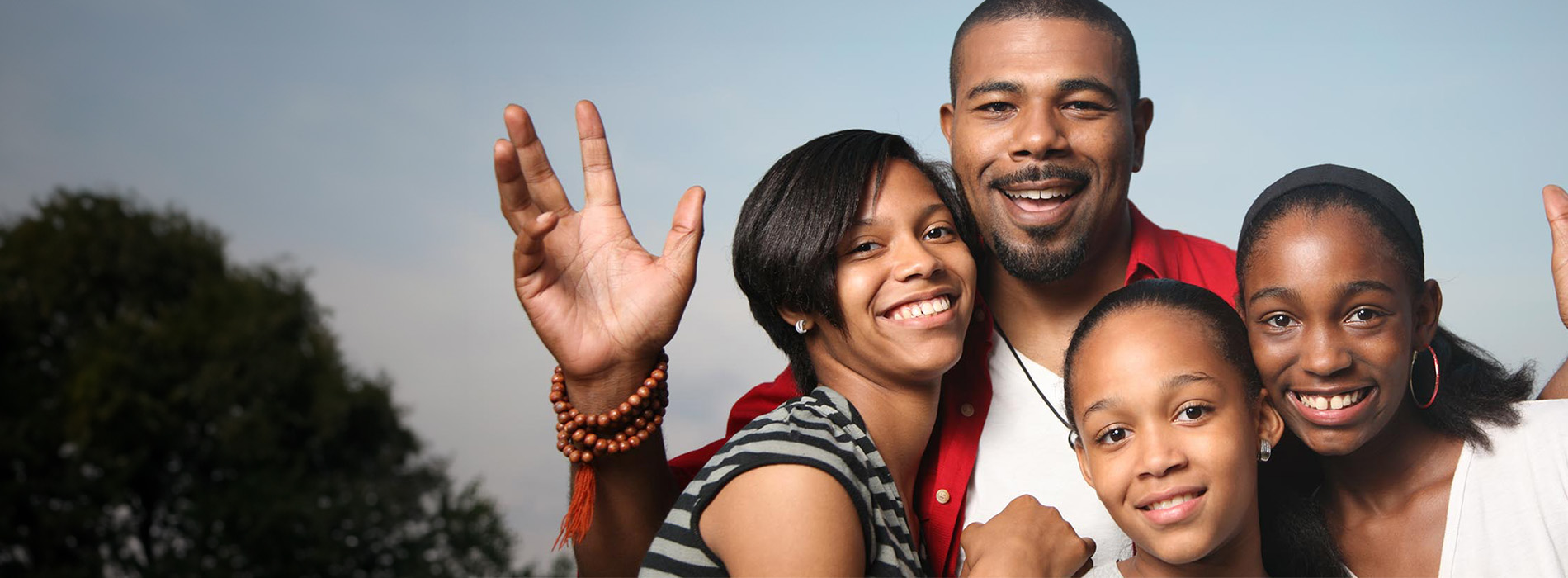The image shows a family of five people posing together with smiles, against a blurred background.
