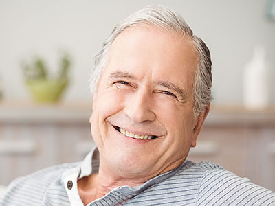 The image shows an elderly man with gray hair, wearing a blue shirt, sitting comfortably with his eyes closed and a slight smile on his face, appearing content and relaxed.